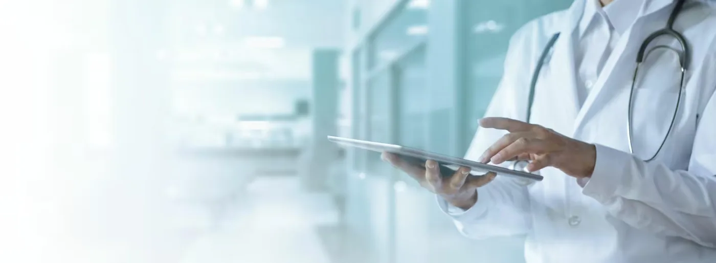 Ärztin im weißen Kittel arbeitet mit einem Tablet in einem hellen Flur.