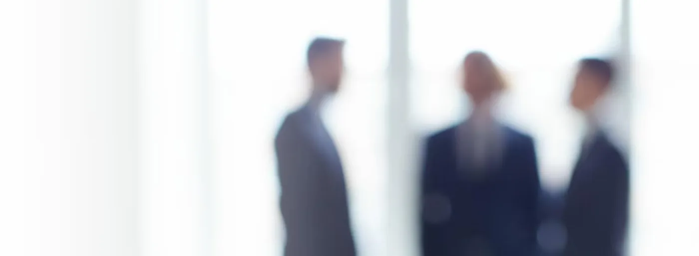 Mehrere Personen in Businesskleidung stehen in einem hellen Büro im Gespräch.