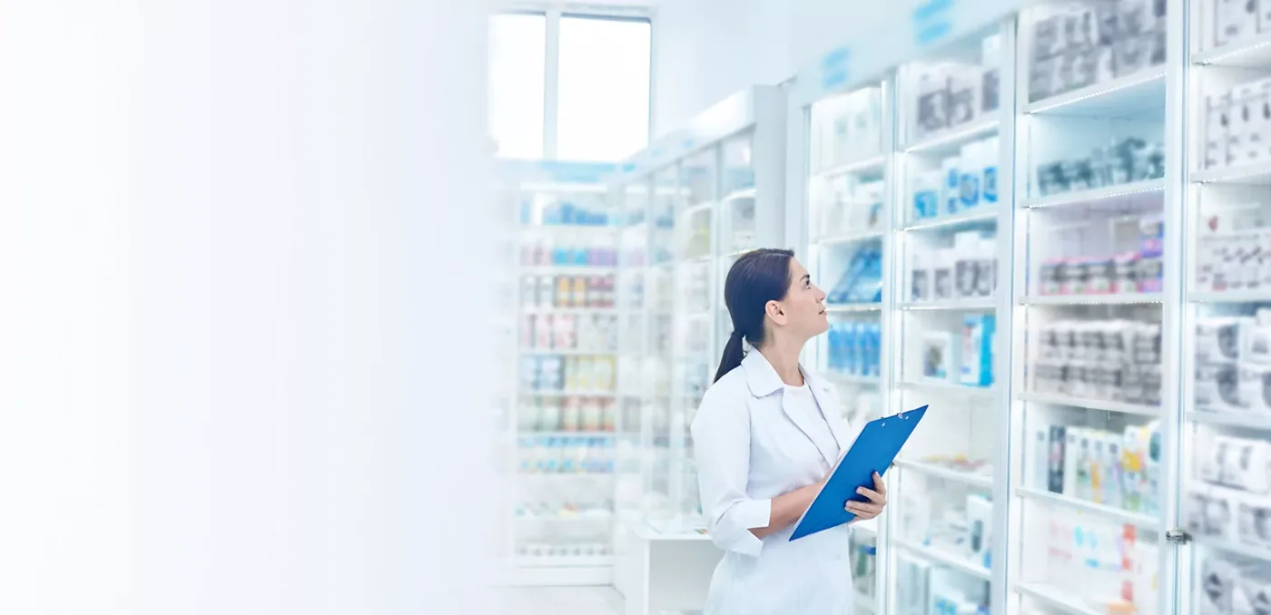 Apothekerin mit Unterlagen vor gefüllten Medikamentenregalen.